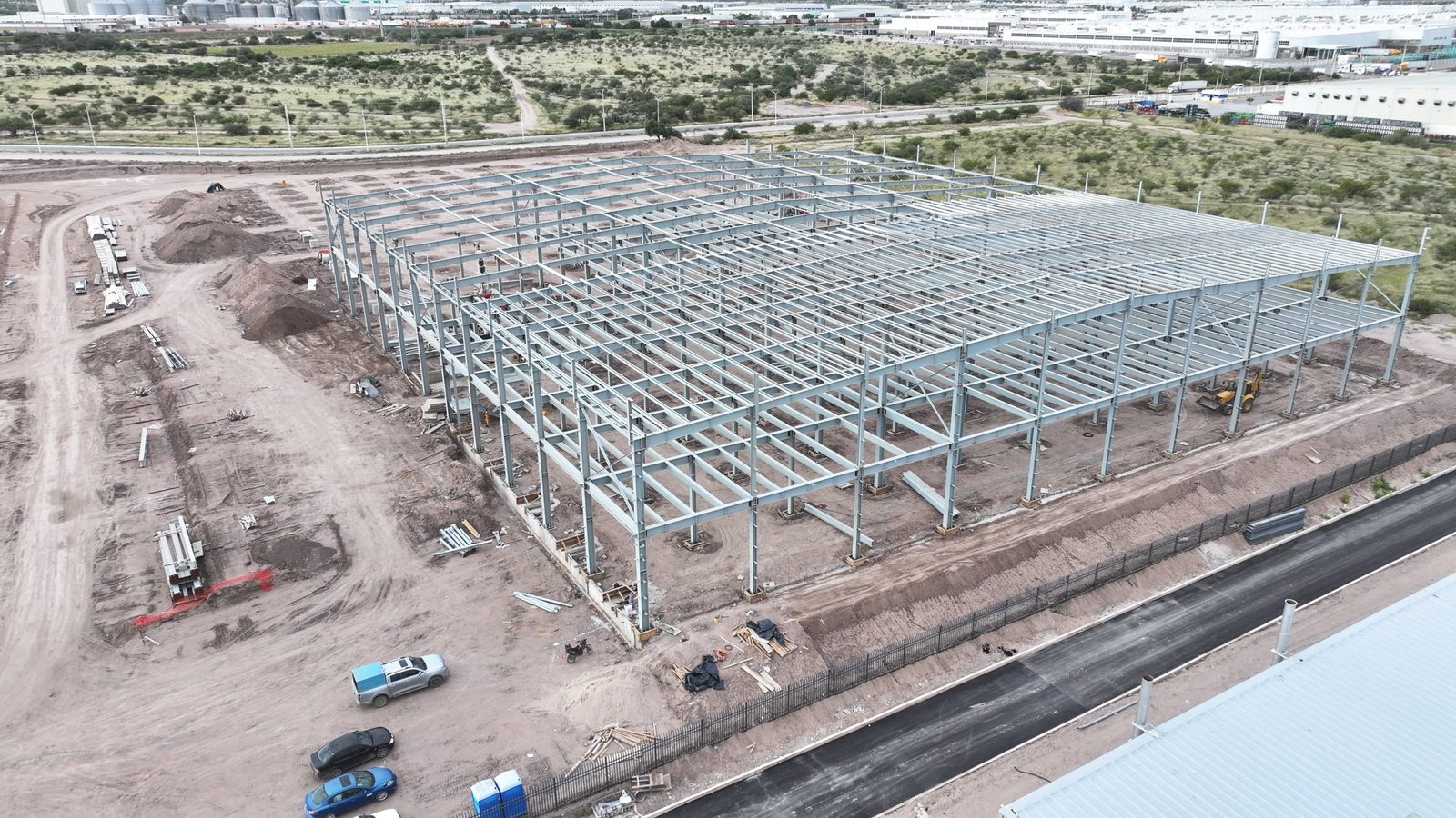 Montaje de estructura met&aacute;lica junto a una nave en operaci&oacute;n con paneles solares